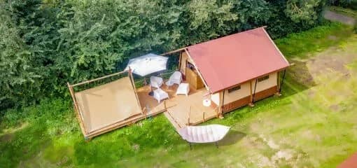 Photo aérienne du Cozy Lodge avec son toit rouge et sa véranda, du Teeny Lodge juste à côté et d'un hamac sur la pelouse