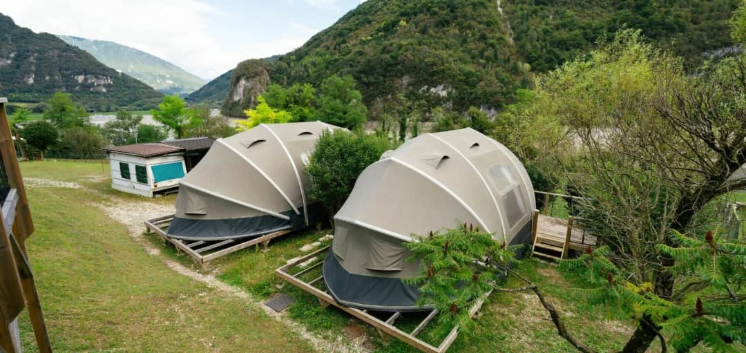 Deux Big Oak Lodges XS, avec une toile de tente en forme de dôme posée sur des caillebotis en bois, nichés au milieu de montagnes verdoyantes aux parois rocheuses