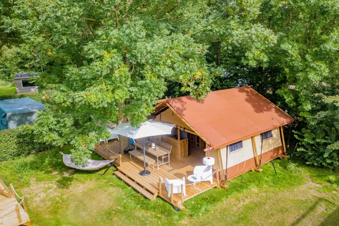 Vue aérienne du Cozy Lodge, avec son toit rouge-brun niché sous de grands arbres, un parasol, une table à manger et un hamac près de la véranda