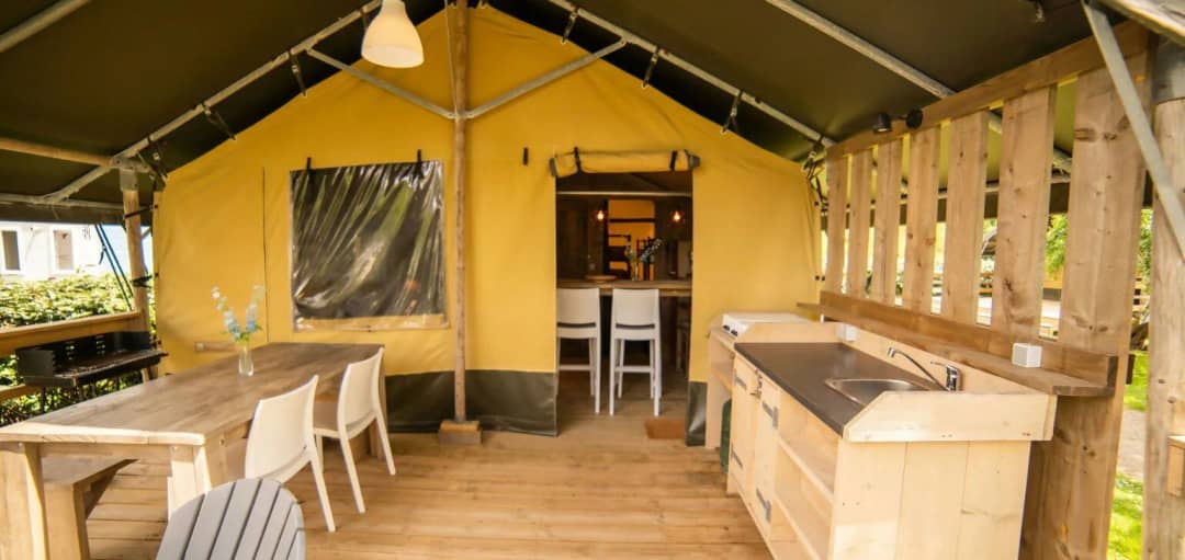 Véranda couverte du Safari Lodge avec table à manger en bois, chaises blanches, cuisine extérieure équipée d'un évier et d'un barbecue