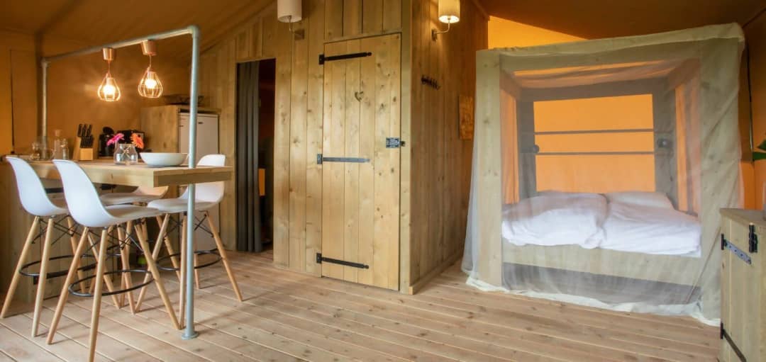 Pièce à vivre du Desert Lodge XL avec bar en bois, tabourets de bar blancs, porte en bois et lit à baldaquin avec moustiquaire