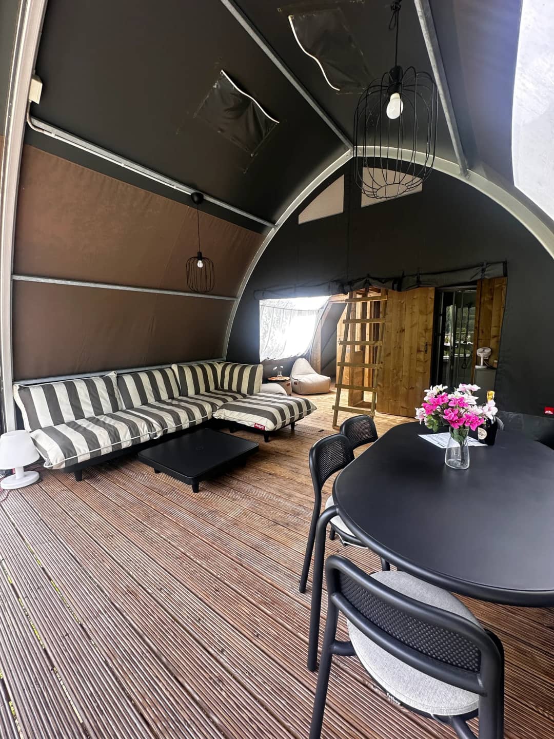 Pièce à vivre du Big Oak Lodge XL avec un canapé de salon rayé, une table à manger noire ornée de fleurs et une échelle en bois