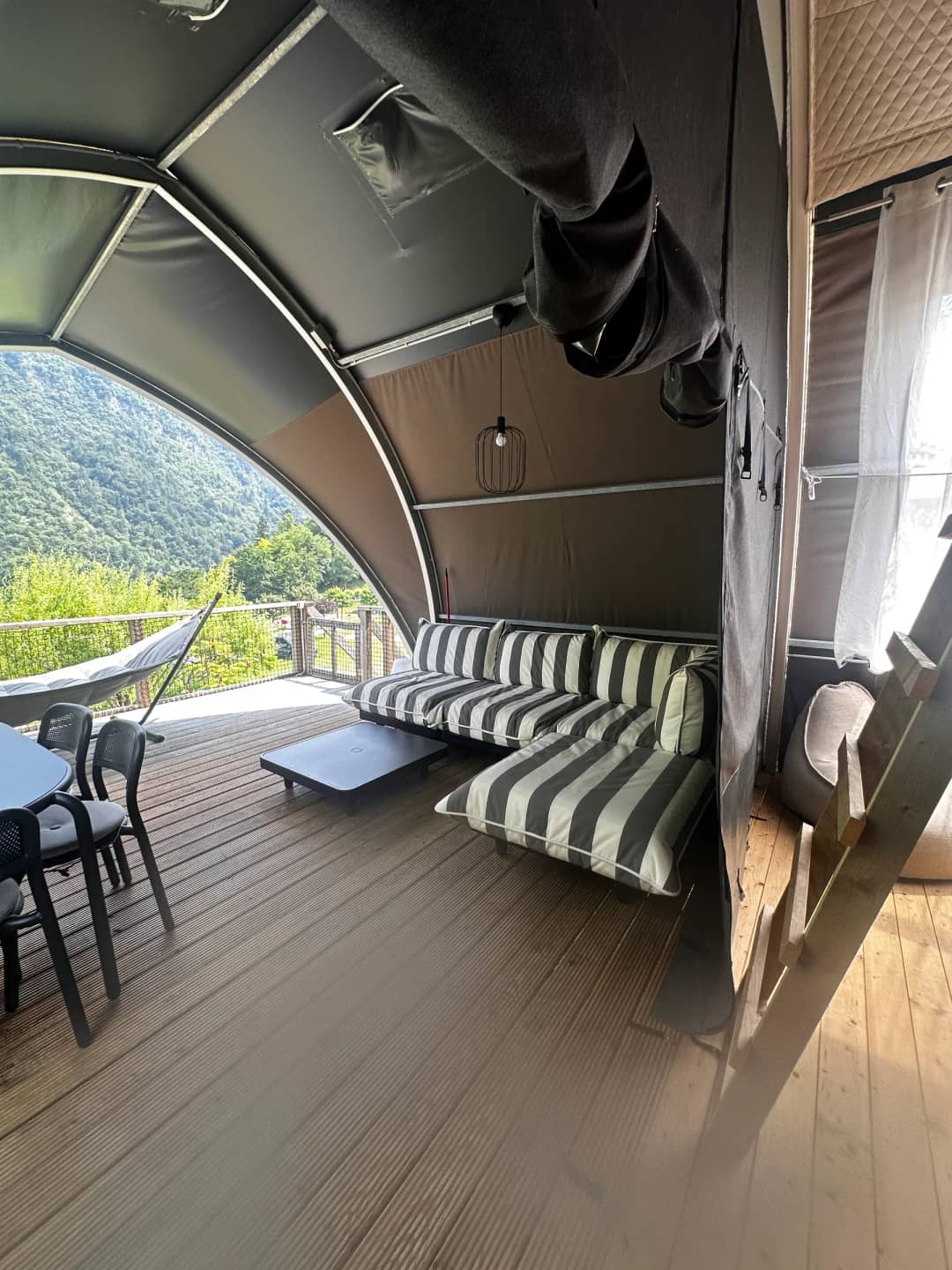 Véranda couverte du Big Oak Lodge XL avec canapé de salon rayé, table basse et table à manger, offrant une vue sur les montagnes