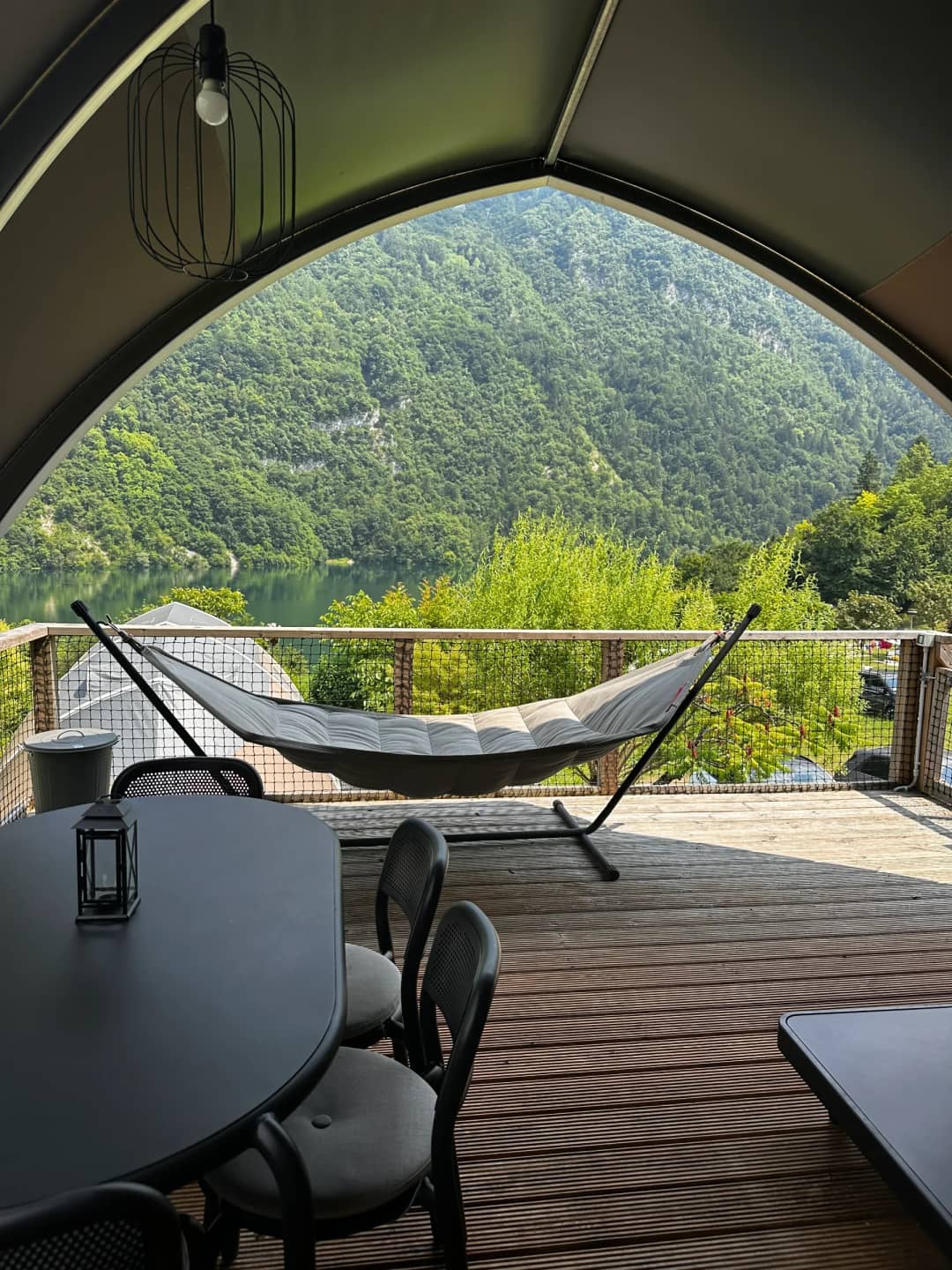 Hamac et table à manger avec lanterne sur la véranda du Big Oak Lodge XL, avec vue sur le lac et les montagnes