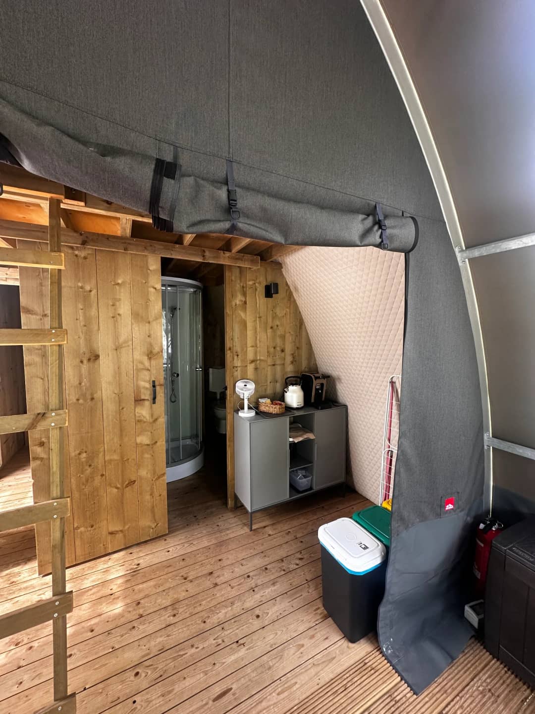 À l'intérieur du Big Oak Lodge XL : une porte en bois menant à la cabine de douche et un petit meuble contenant une bouilloire et un grille-pain